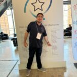 Sylvain montrant du doigt son nom sur les murs de tableau IBM champion